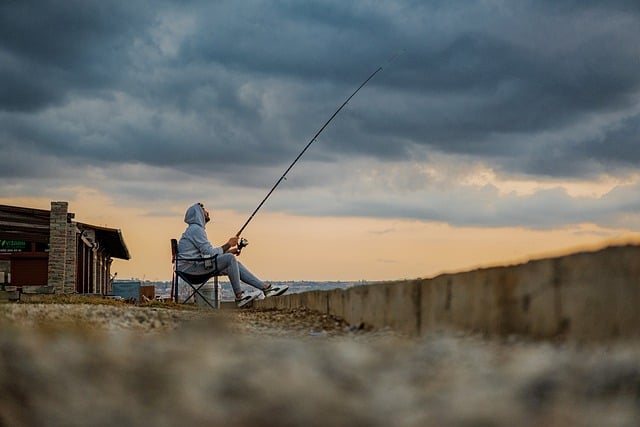 A man sitting on a bench in Brooklyn with a fishing rod, engaging in legal fishing activity.